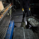 A worker pushes a wheelbarrow with broken glass bottles while new Coke bottles move along the conveyor belt.